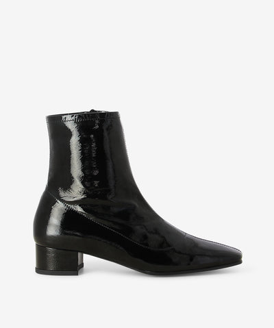 Black patent leather ankle boots by Sempre Di. It features a paneled upper with side zip closure, low block heel, and a chisel toe.