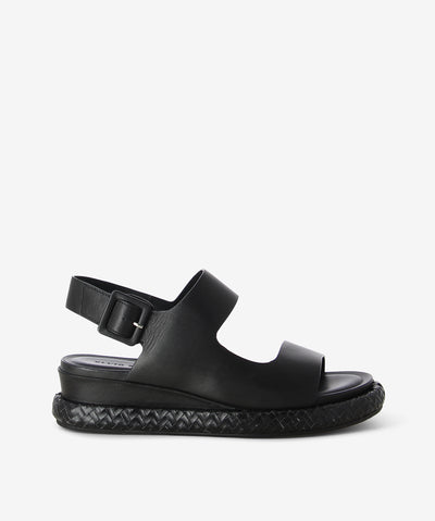 Black leather sandals by Elvio Zanon. It features an asymmetrical upper with an adjustable pin-buckle fastening, woven effect midsole, and a round toe.