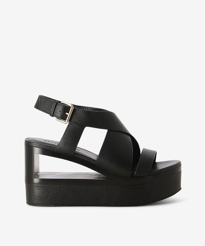 Black platform sandals by Elvio Zanon. It features a crossed upper with a buckle back strap, a platform cutout heel and almond toe.