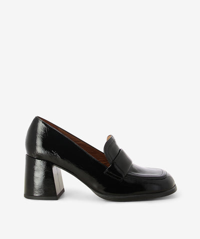 Black crinkle patent leather heeled loafers by Neo. It is a slip on style and features a block heel, padded upper strap, and a soft square toe.