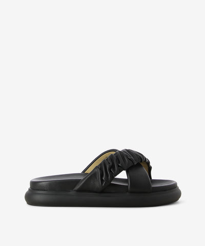 Black leather slides by 2 Baia Vista. It is a slip on style and features ruched cross straps, a raised padded sole, and a round toe.