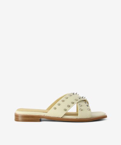 Off-white leather slides by 2 Baia Vista. It is a slip on style and features cross straps with stud embellishments, low block heel, and a square toe.