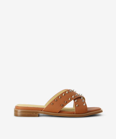 Tan leather slides by 2 Baia Vista. It is a slip on style and features cross straps with stud embellishments, low block heel, and a square toe.