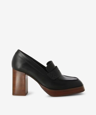 A classic penny silhouette black leather heeled loafers by Alohas. A slip-on style features a wooden block heel and a square toe.