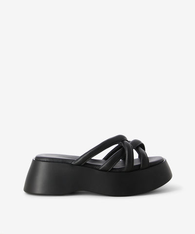 Black leather slides by 2 Baia Vista. It is a slip-on style that features multiple crossover straps as its upper, a platform sole, and a rounded toe. 