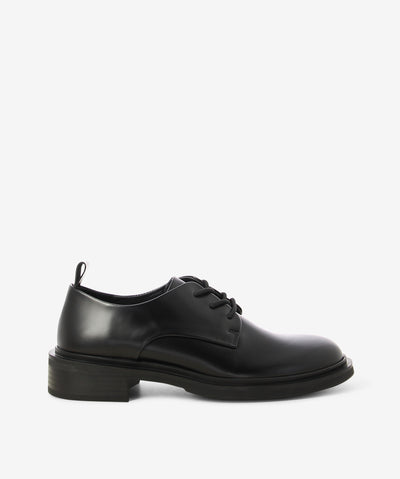 Black hi-shine derby shoes by EOS. It is a lace-up style and features a rear pull tab, low block heel, and a round toe.