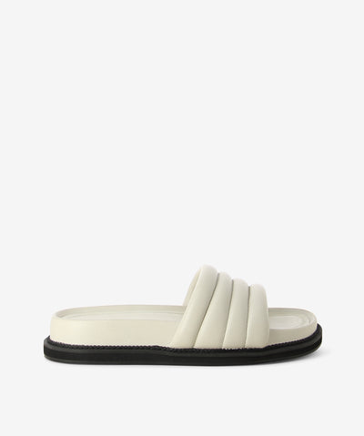 White leather cushion slides by AJ Projects. It is a slip-on style and features a padded leather band, a moulded footbed and a round toe.