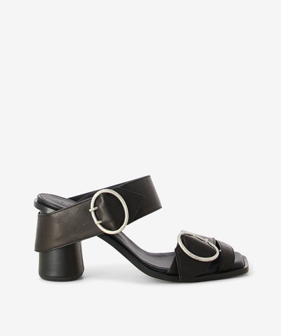 Black premium nappa leather heeled sandals by Beau Coops. It has an antique silver oval buckled strap with buckles with wrap around heel and features an oval block heel and a soft square toe.