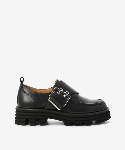 Black leather loafers by EOS. It features a wide strap with a double pin-buckle fixture, chunky tread sole, and a round toe.&nbsp;