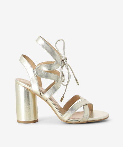 Platinum metallic leather heeled sandals by Bruno Premi. It features a strappy geometric upper with tie up fastening, high round block heel, and a round toe.