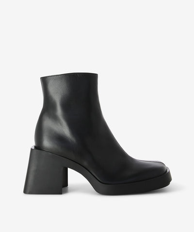 Black leather ankle boot by Justine Clenquet. Is a slip-on style and features inner zip, rubber platform sole, block heel and a square toe.