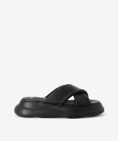 Black leather slides by Rollie. It is a slip-on style that features two crossover straps, a moulded footbed, a platform sole, and a round toe. 