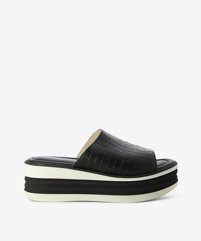 Black and white leather platform slides by Origini Studio. It is a slip on style and features a weave effect upper, platform sole, and a round toe.